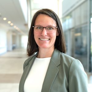 Headshot of Dr. Erin Mazerolle. She is a white woman who has shoulder length brunette hair, glasses, and is wearing a green blazer.
