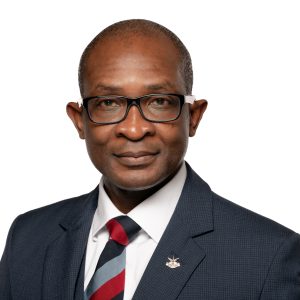 Headshot of Dr. Felix Odartey-Wellington. He is a Black man who shaves his head, had black glasses, and is wearing a navy blazer and red tie.