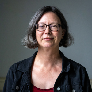 Headshot of instructor Terra Tailleur. She is a white woman who has dark chin length hair, black glasses, and is wearing a black collared jacket.